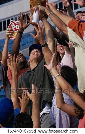 Stock Image - Low angle view of a group of spectators reaching out for a baseball in a stadium. Fotosearch