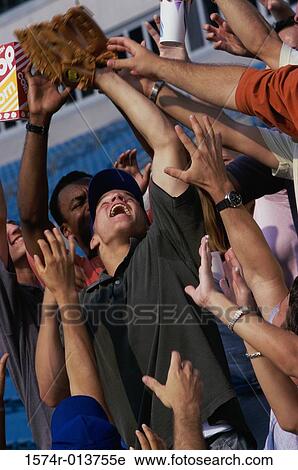 Stock Image - Low angle view of a group of spectators reaching out for a baseball in a stadium. Fotosearch