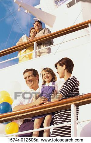 Stock Image - Low angle view of a mid adult couple with their daughter standing on the deck of a cruise ship smiling. Fotosearch