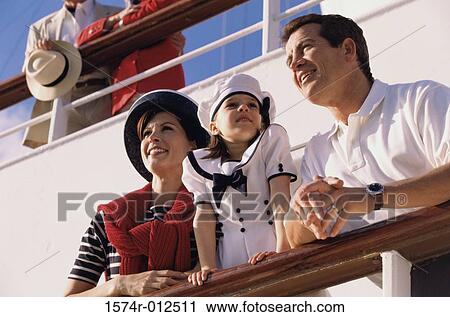 Stock Image - Low angle view of a mid adult couple with their daughter standing on the deck of a cruise ship. Fotosearch
