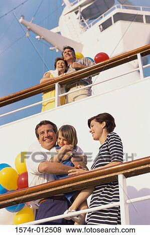 Stock Photo - Low angle view of a mid adult couple with their daughter standing on the deck of a cruise ship smiling. Fotosearch