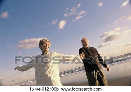 Stock Image - Low angle view of a senior couple standing on the beach. Fotosearch