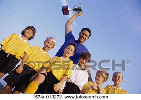 Low angle view of a sports team with their coach standing behind them holding a trophy View Large Photo Image Stock Image - Low angle view of a sports team with their coach standing behind them holding a trophy. Fotosearch