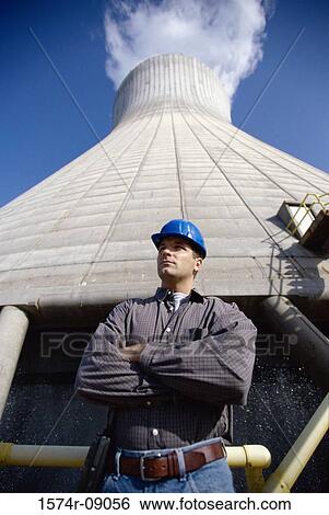 Stock Photograph - Low angle view of a worker standing beside a smoke stack at a power plant. Fotosearch