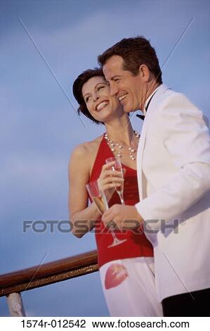 Stock Image - Low angle view of a young couple holding champagne flutes on the deck of a cruise ship. Fotosearch