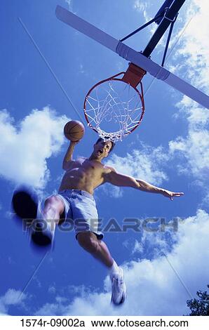 Stock Image - Low angle view of a young man slam dunking a basketball. Fotosearch