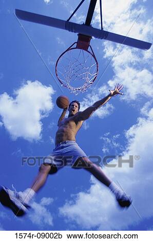 Stock Image - Low angle view of a young man slam dunking a basketball. Fotosearch