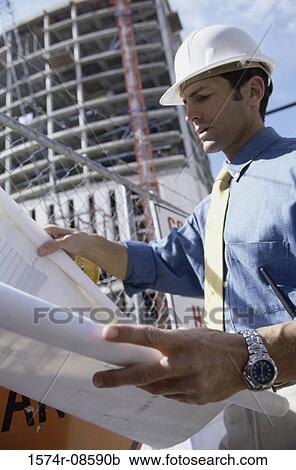 Stock Image - Low angle view of an engineer at a construction site holding blueprints. Fotosearch