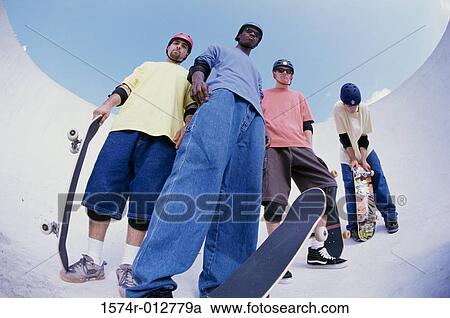 Low angle view of four young men standing with skateboards View Large Photo Image Stock Image - Low angle view of four young men standing with skateboards. Fotosearch