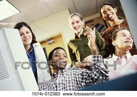 Stock Image - Low angle view of high school students in front of a computer in a classroom. Fotosearch