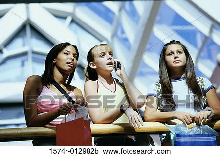 Stock Image - Low angle view of three teenage girls standing in a shopping mall. Fotosearch