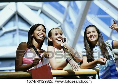 Stock Image - Low angle view of three teenage girls standing in a shopping mall. Fotosearch