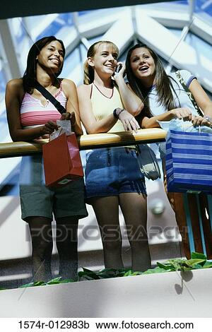 Stock Image - Low angle view of three teenage girls standing in a shopping mall. Fotosearch