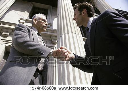 Stock Image - Low angle view of two businessmen shaking hands. Fotosearch