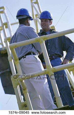 Low angle view of two construction workers discussing View Large Photo Image Stock Photography - Low angle view of two construction workers discussing. Fotosearch