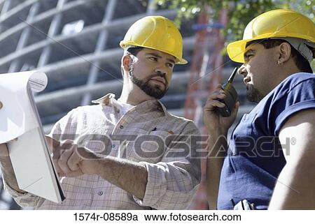 Low angle view of two foremen working at a construction site View Large Photo Image Stock Image - Low angle view of two foremen working at a construction site. Fotosearch