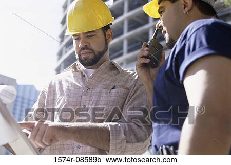 Stock Image - Low angle view of two foremen working at a construction site. Fotosearch