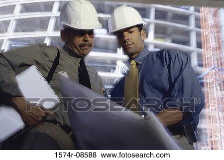 Low angle view of two foremen working on blueprints at a construction site View Large Photo Image Stock Photo - Low angle view of two foremen working on blueprints at a construction site. Fotosearch