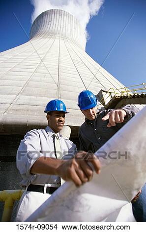 Low angle view of workers standing beside a smoke stack at a power plant looking at blue prints View Large Photo Image Picture - Low angle view of workers standing beside a smoke stack at a power plant looking at blue prints. Fotosearch