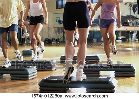 Stock Image - Low section view of a group of people doing step aerobics in a gym. Fotosearch