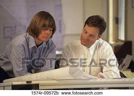 Stock Image - Male and female architects working on blueprints. Fotosearch