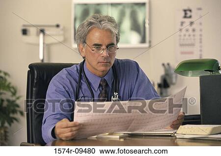 Stock Image - Male doctor seated behind a desk reading. Fotosearch