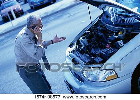 Stock Photo - Man standing in front of a broken down car talking on a mobile phone. Fotosearch