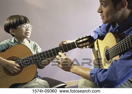 Stock Image - Man teaching a boy how to play the guitar. Fotosearch
