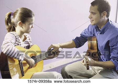 Stock Image - Man teaching a girl how to play the guitar. Fotosearch