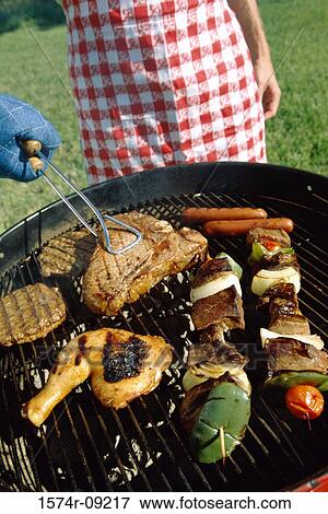 Stock Photo - Man using tongs on meat cooking in a barbecue grill. Fotosearch