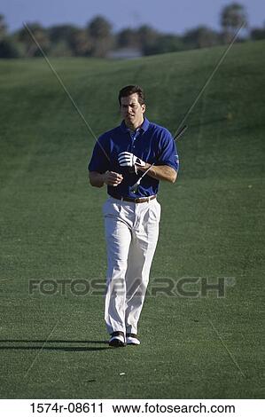 Stock Image - Man walking with a golf club on a golf course. Fotosearch