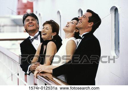 Stock Image - Mature couple and a mid adult couple standing on the deck of a cruise ship laughing. Fotosearch