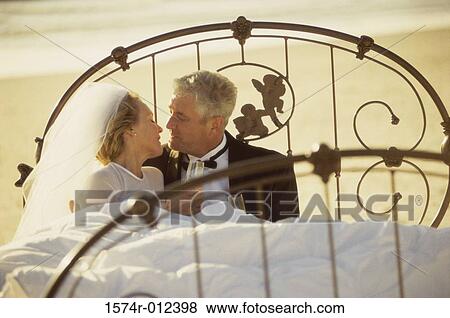 Stock Photo - Mature couple holding champagne flutes on a bed. Fotosearch