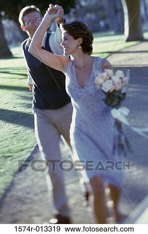 Stock Photo - Mature couple holding hands running on a lawn. Fotosearch