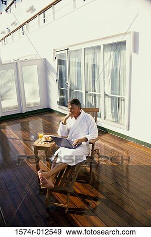 Stock Photo - Mature man sitting in a deck chair with a laptop. Fotosearch