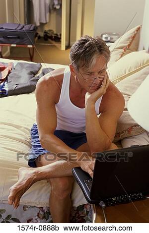 Mature man sitting on the bed and using a laptop View Large Photo Image Stock Image - Mature man sitting on the bed and using a laptop. Fotosearch