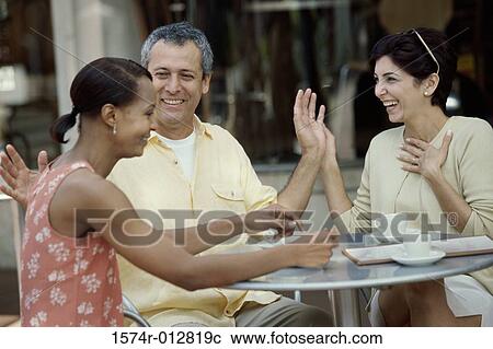 Mid adult couple and a young woman sitting together in a cafe View Large Photo Image Stock Image - Mid adult couple and a young woman sitting together in a cafe. Fotosearch