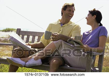 Stock Image - Mid adult couple sitting on a bench and laughing. Fotosearch