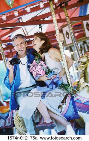 Mid adult couple sitting on a carousel horse View Large Photo Image Stock Image - Mid adult couple sitting on a carousel horse. Fotosearch