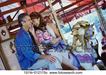 Stock Image - Mid adult couple sitting on a carousel horse. Fotosearch