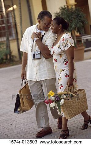 Mid adult couple walking on a sidewalk holding shopping bags View Large Photo Image Stock Image - Mid adult couple walking on a sidewalk holding shopping bags. Fotosearch