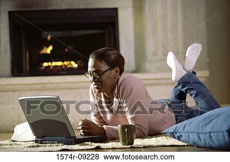 Stock Photo - Mid adult woman lying on the floor in front of a laptop. Fotosearch