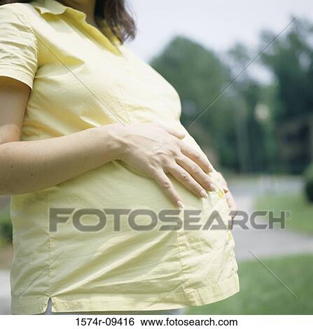 Mid section view of a pregnant woman touching her abdomen View Large Photo Image Stock Photograph - Mid section view of a pregnant woman touching her abdomen. Fotosearch