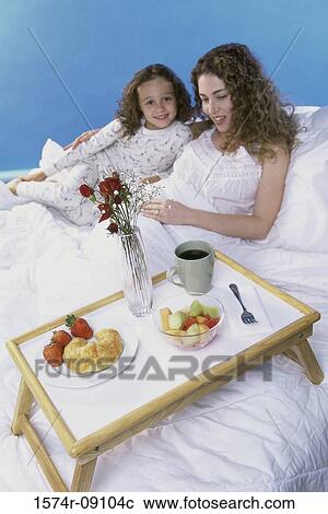 Stock Image - Mother and daughter in bed together with a breakfast tray. Fotosearch