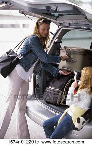 Stock Image - Mother and her daughter loading luggage into the back of a car. Fotosearch