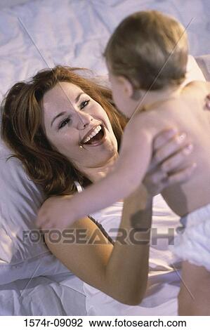 Stock Image - Mother lying in bed holding her baby boy. Fotosearch