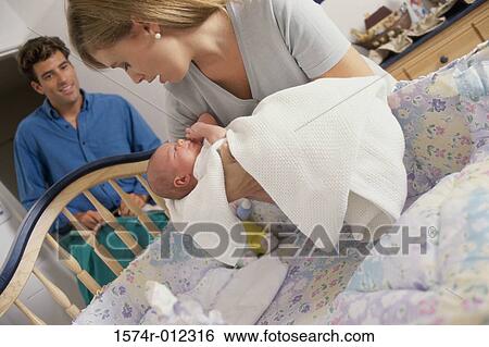 Stock Photograph - Mother placing her son in a crib. Fotosearch