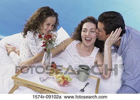 Stock Image - Parents and their daughter in bed with a breakfast tray. Fotosearch