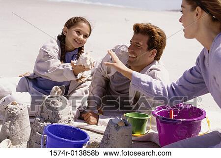 Stock Image - Parents and their daughter making a sand castle on the beach. Fotosearch