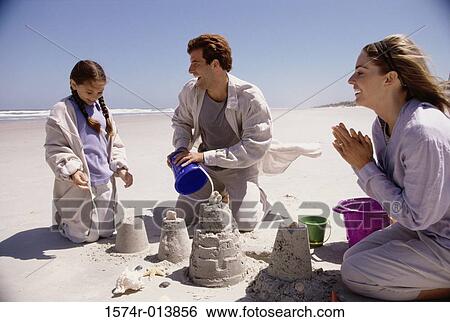 Stock Photograph - Parents and their daughter making a sand castle on the beach. Fotosearch